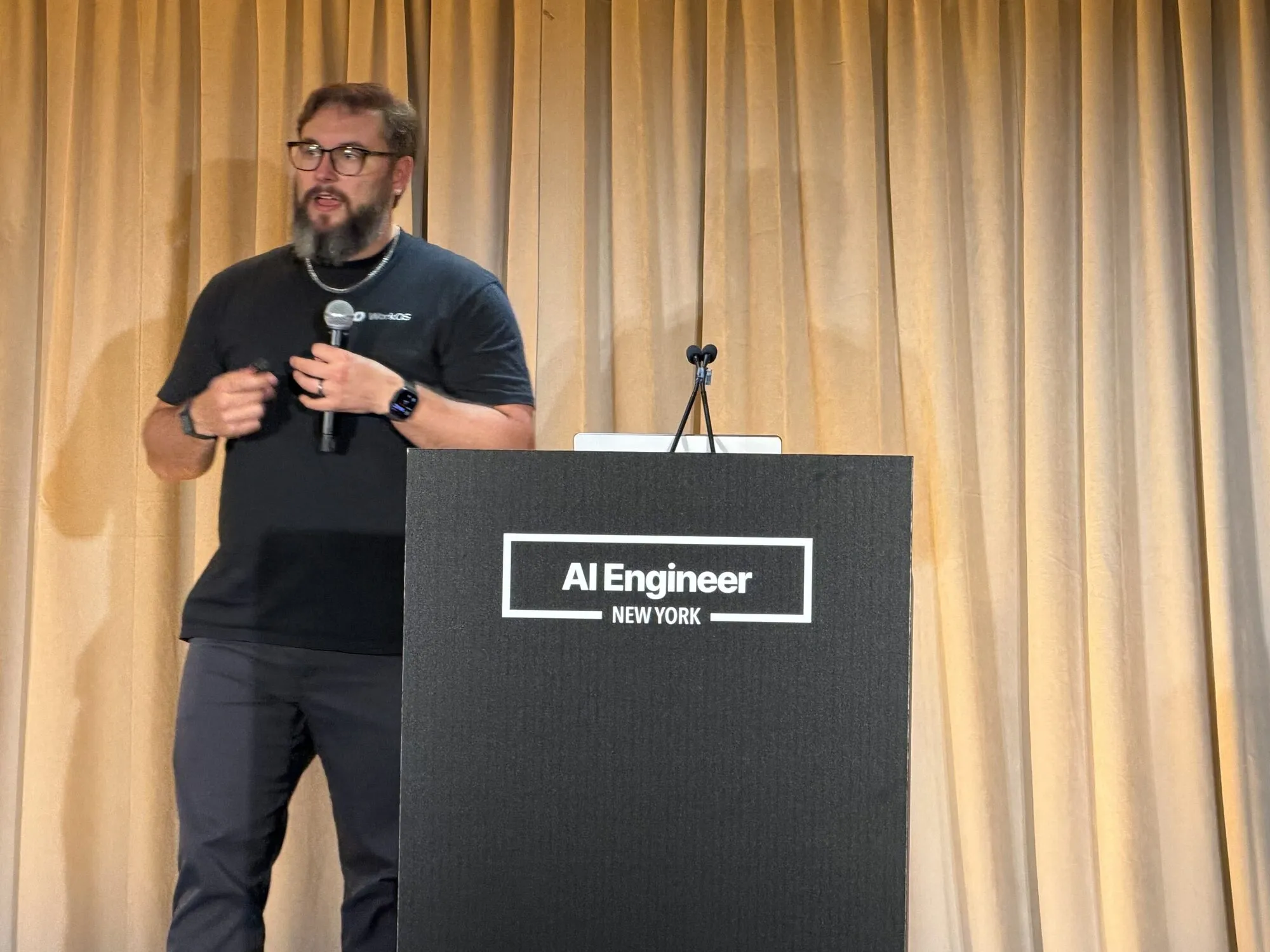 Nick on stage at AI Engineer New York, holding a microphone next to the AI Engineer New York podium.